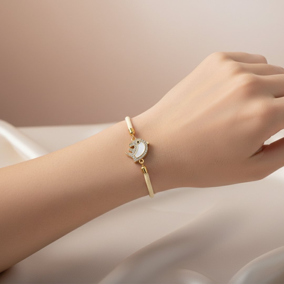 Poignet d'une femme portant un bracelet en cordon de couleur crème, orné d'un pendentif doré en forme d'éléphant. Le corps de l'animal est en nacre blanche, et son contour est serti de petits cristaux scintillants.