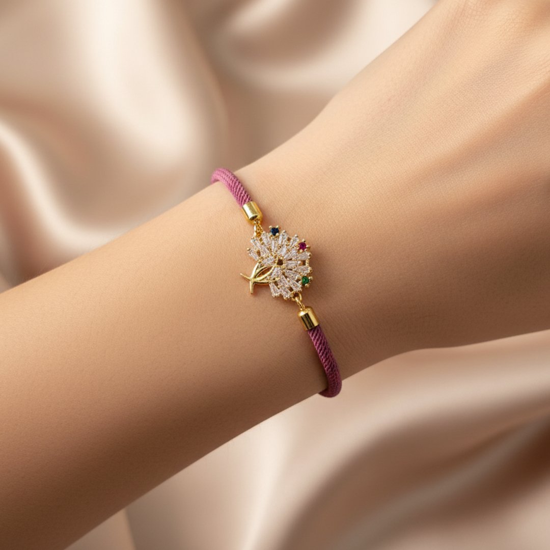 Poignet d'une femme portant un bracelet en cordon de couleur mauve. Le pendentif doré représente un arbre de vie stylisé, avec une moitié entièrement pavée de cristaux blancs et l'autre moitié en or poli ornée de cristaux multicolores symbolisant les fruits.