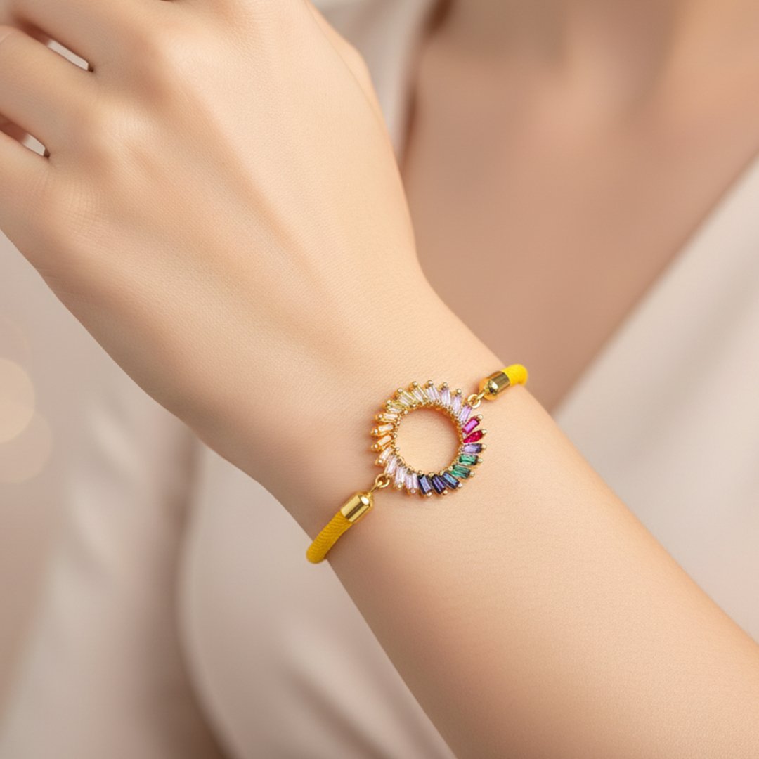 Poignet d'une femme portant un bracelet en cordon jaune vif avec un médaillon circulaire doré. Le médaillon est serti de pierres multicolores de taille baguette, disposées en un dégradé arc-en-ciel.