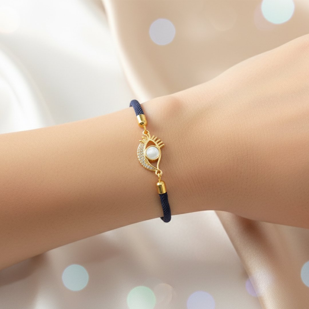 Poignet d'une femme portant un bracelet en cordon bleu nuit. Le pendentif doré est un œil protecteur stylisé, avec une partie en croissant pavée de cristaux blancs et un centre en nacre blanche.