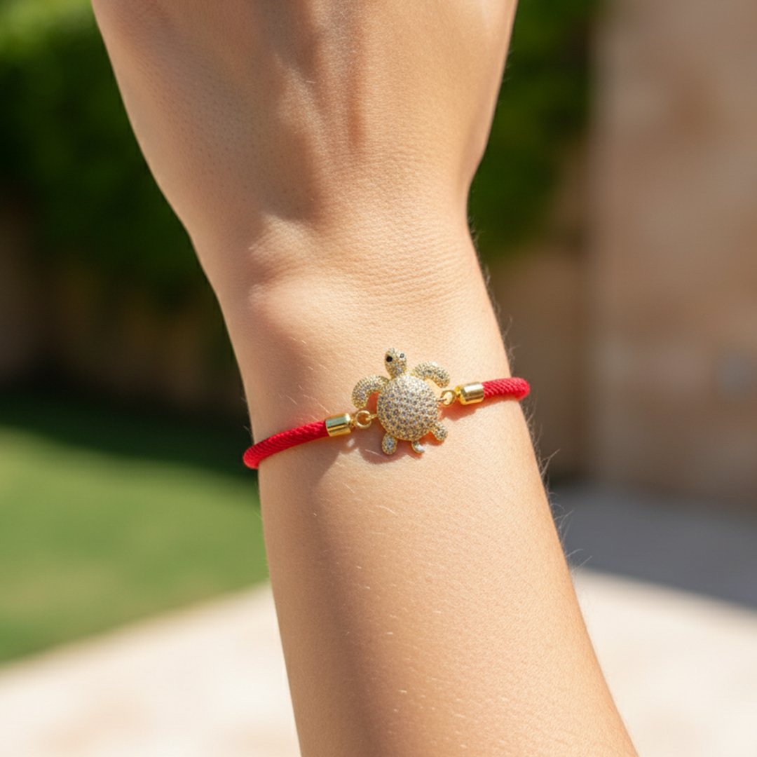 un bracelet en cordon rouge vif, orné d'un pendentif en forme de tortue marine dorée et entièrement pavé de cristaux blancs scintillants.